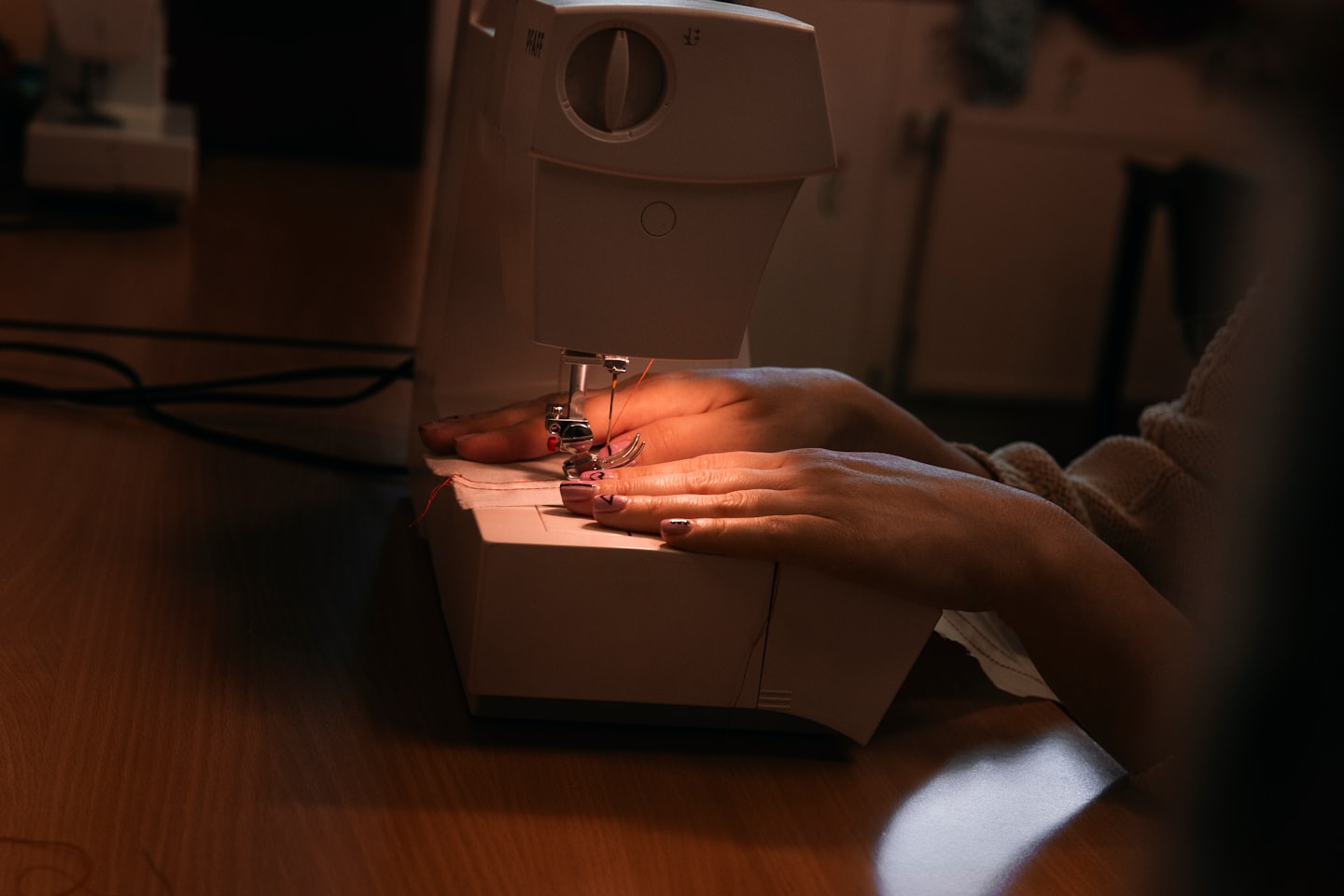 Manos guiando hilo rojo a través de una máquina de coser blanca.
